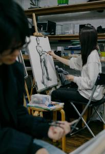 Two art students sketching a nude figure in a Tokyo studio, focused on improving their drawing skills.